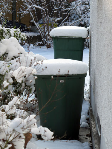 Dos depósitos verdes de agua de lluvia cubiertos de nieve junto a la pared en invierno