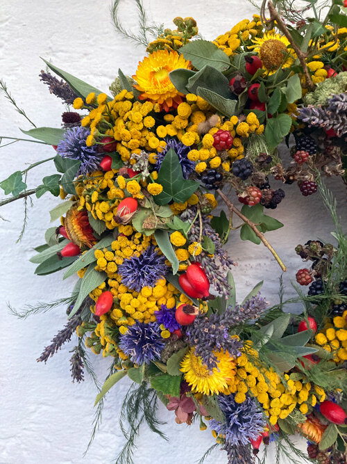 Detalle de una corona otoñal con flores amarillas y azules, escaramujos rojos y bayas oscuras