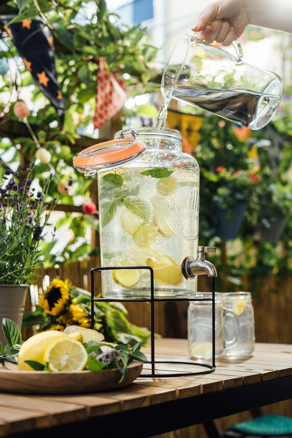 Agua vertida en un dispensador con limón y menta, limonada casera en el balcón
