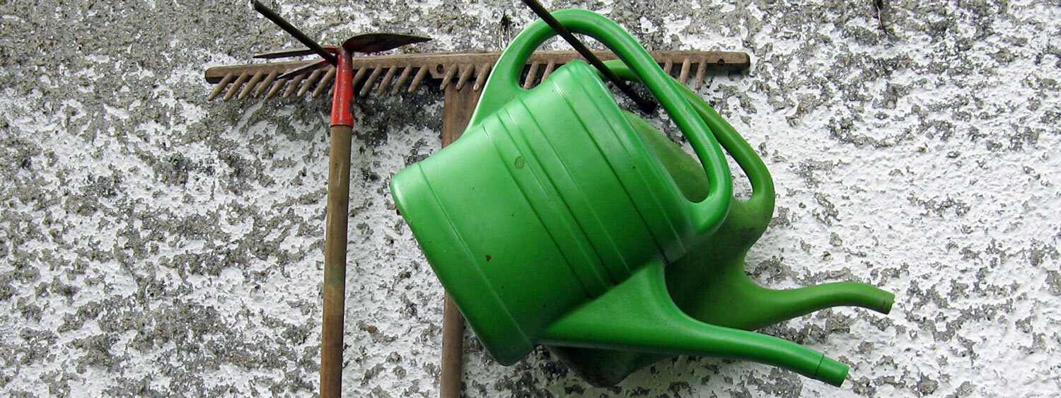 Dos regaderas verdes y un rastrillo colgados en una pared