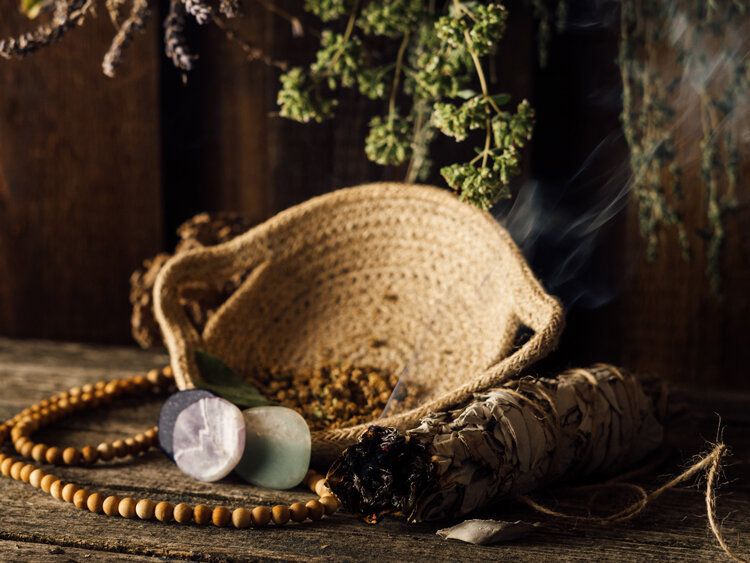 Atado de salvia humeante junto a un cuenco, piedras y un collar de cuentas de madera