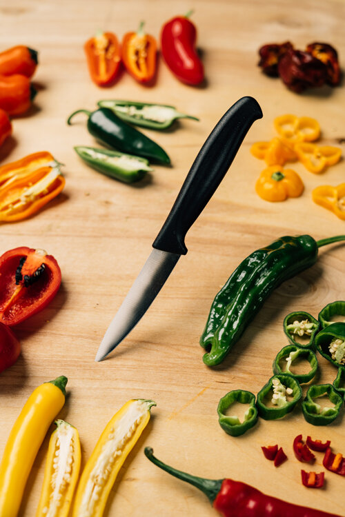 Guindillas cortadas rojas, amarillas, naranjas y verdes con un cuchillo sobre una tabla